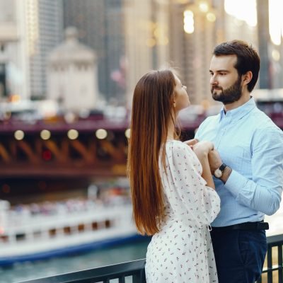 elegant couple in a city beautiful long-haired girl in summer dress with her handsome husband in white shirt and pants standing in sunny Chicago near river